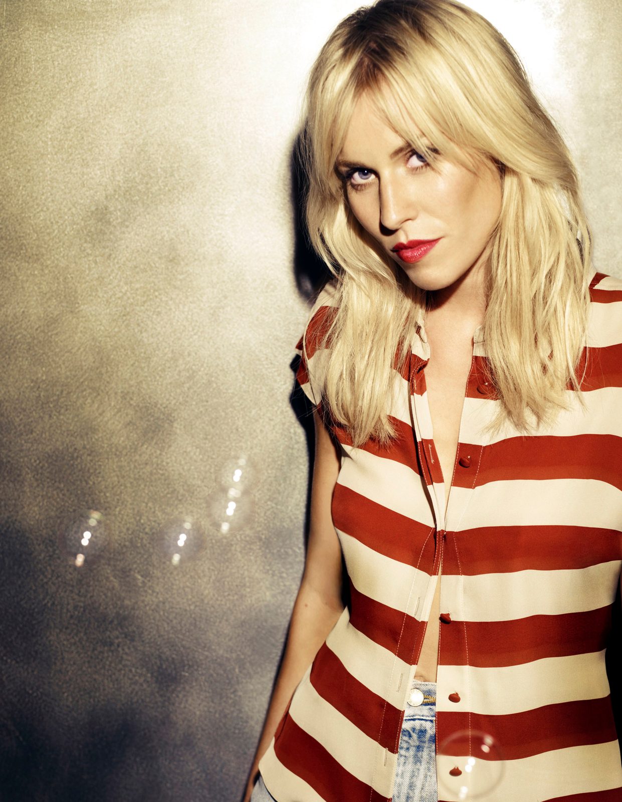 Natasha Bedingfield with tousled blonde hair and red lips in a red and cream striped top against a smoky backdrop