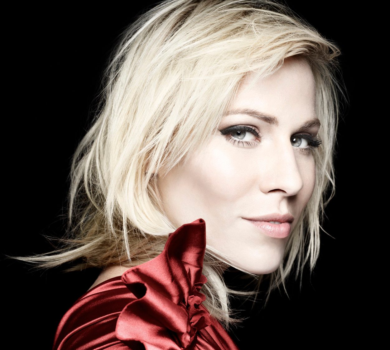 Natasha Bedingfield in close-up with tousled platinum hair and a red satin collar against a black background