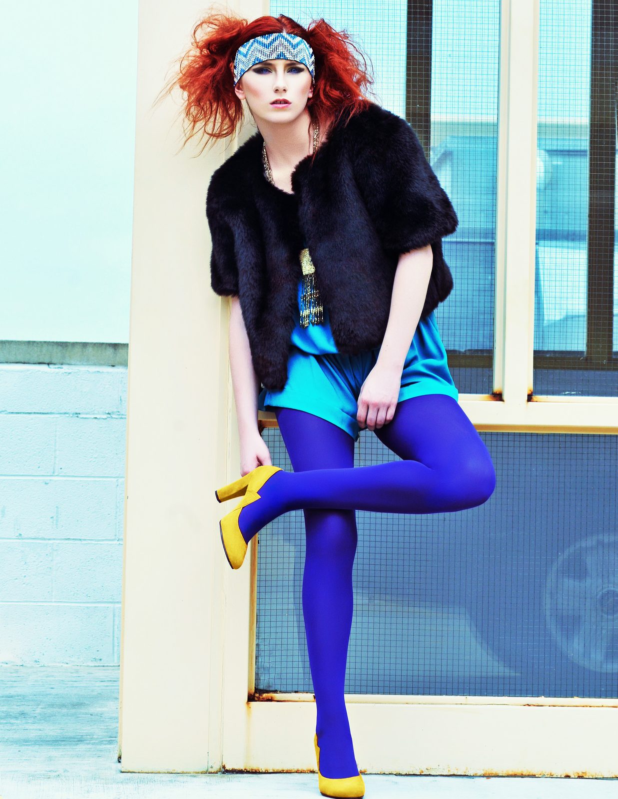 Red-haired model in a fur coat, teal jumpsuit, cobalt tights and yellow heels