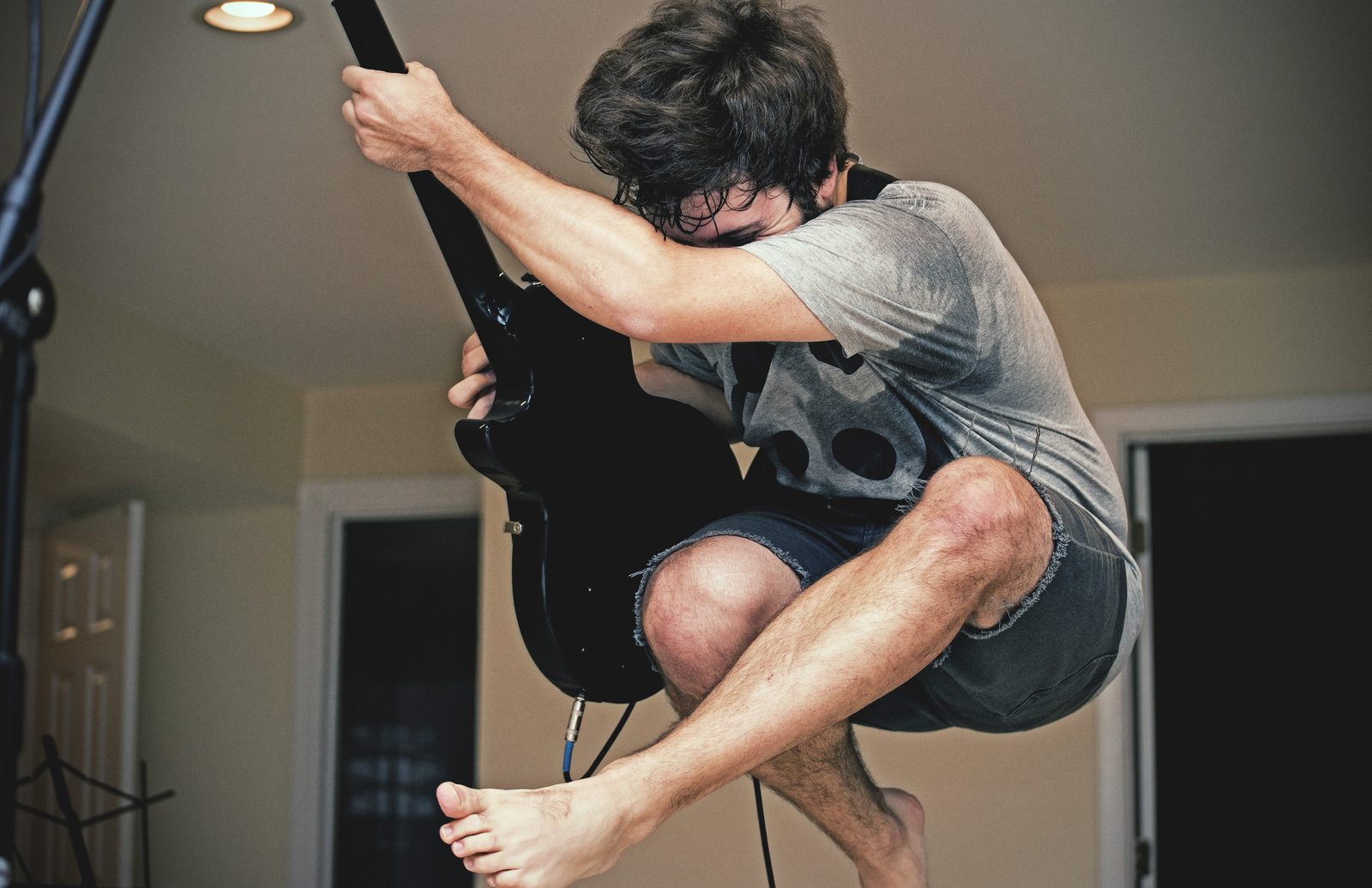 Barefoot Kill Lincoln guitarist in a grey tee and cutoffs leaping mid-air, knees tucked, face buried in his arm as he clutches a black guitar