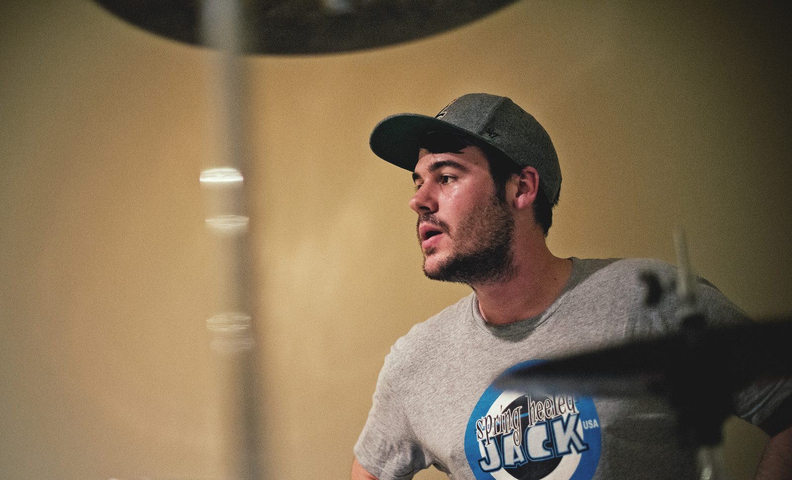 Kill Lincoln’s drummer in a grey baseball cap and graphic tee, mid-song behind a cymbal