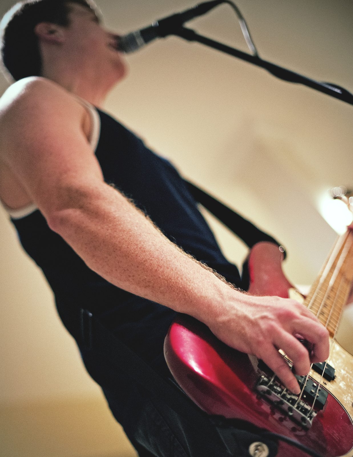 A Kill Lincoln bassist in a black tank top singing into a mic, shot from below as he plays a red bass