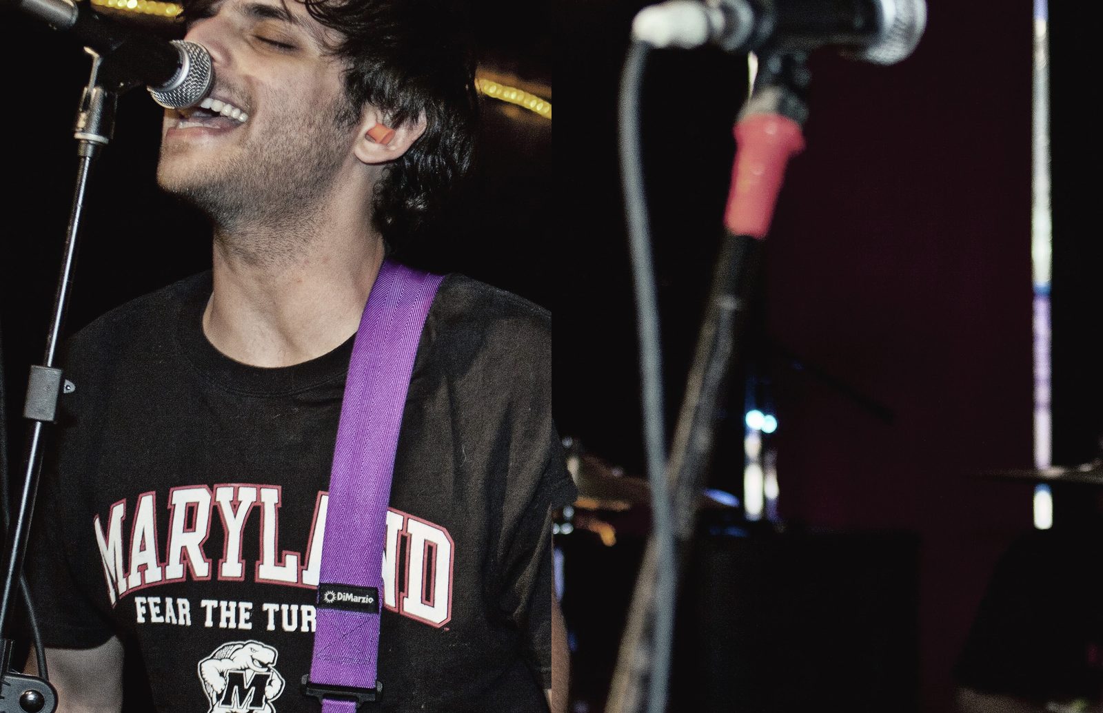 Boardroom Heroes’ singer in a black Maryland tee and purple guitar strap singing into a mic, the drummer in the shadows behind