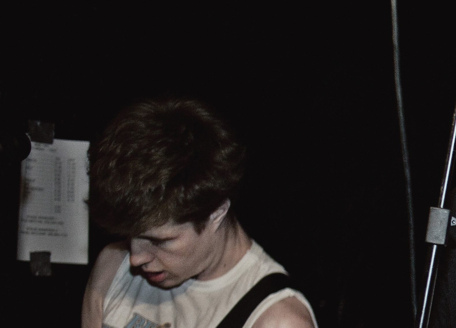 A Boardroom Heroes guitarist in a white tank top, head bowed over his instrument in a dark club