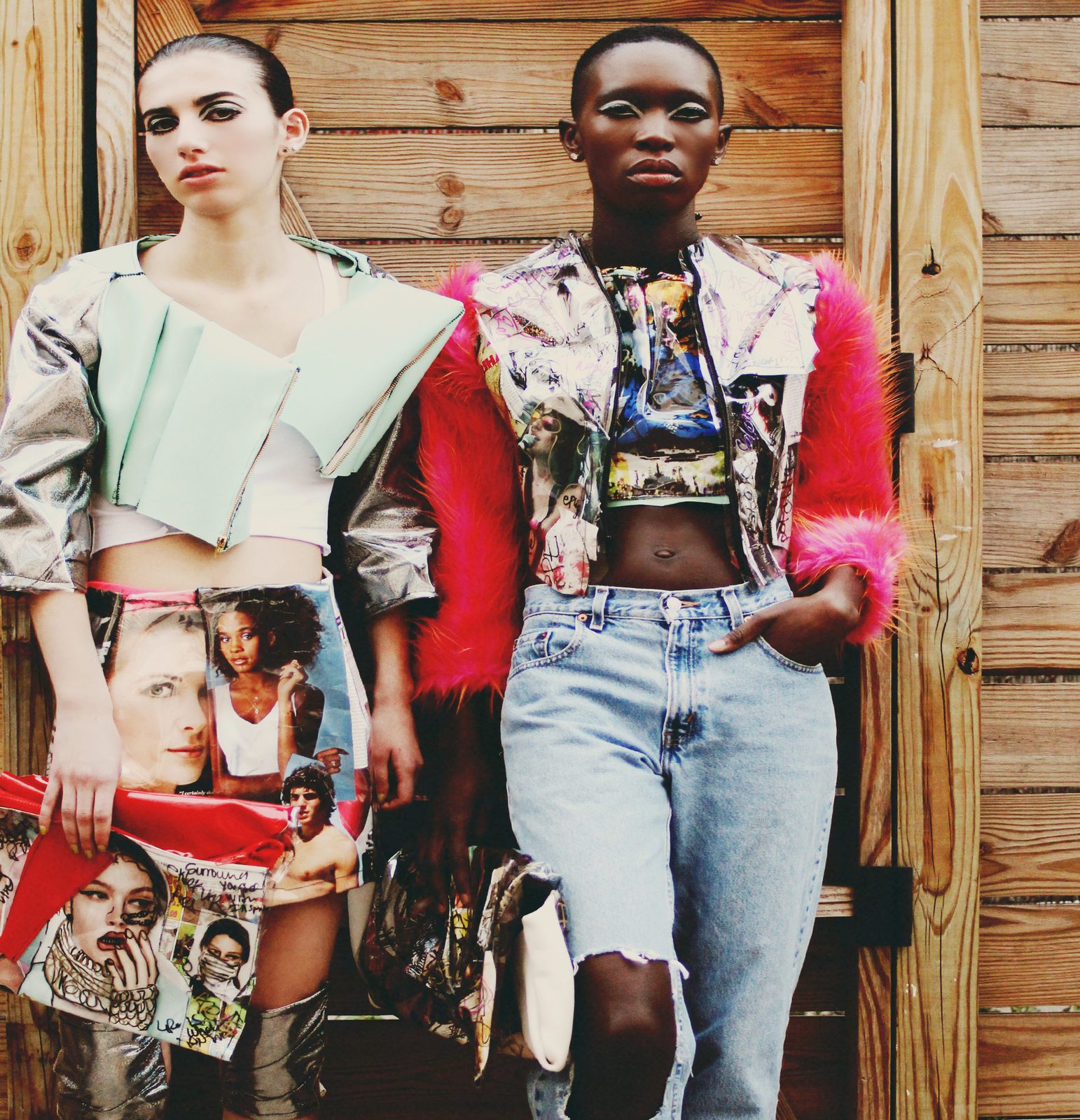 Two models against a wooden fence, one in a mint cropped jacket holding a magazine collage clutch, the other in a collage jacket with hot pink faux fur sleeves and light wash jeans