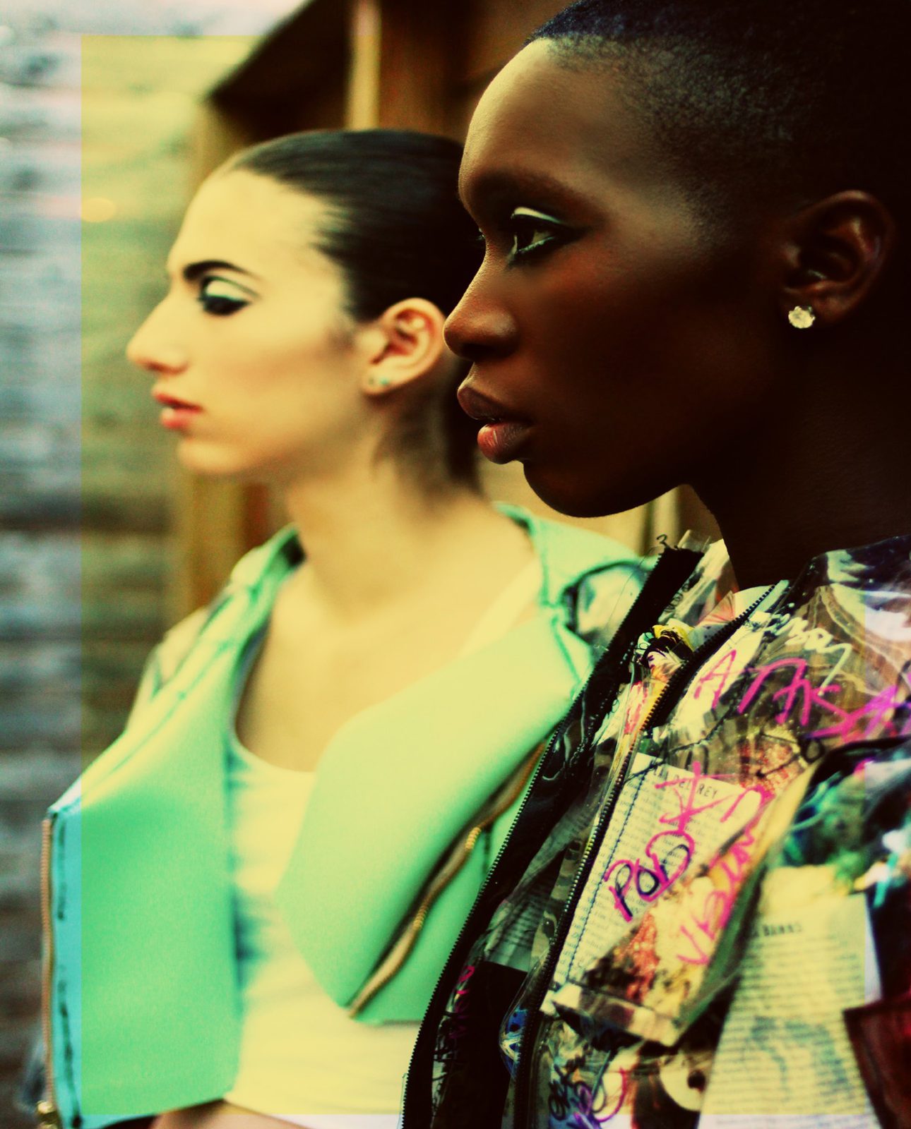 Two models in profile, one in a mint jacket and white tank, the other in a graffiti print collage jacket, shot in saturated color