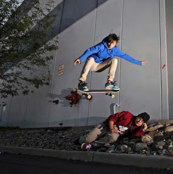 Skateboarder Jennifer Soto in a blue hoodie launching off a wall ramp, a photographer crouched below
