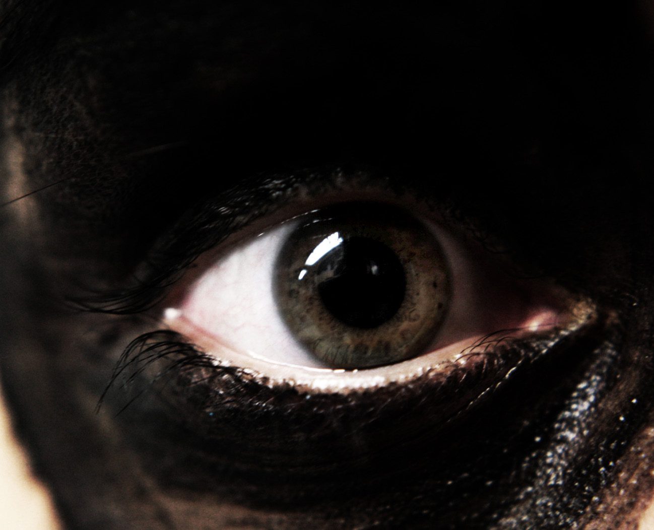 Extreme close-up of a hazel eye ringed in smudged black makeup