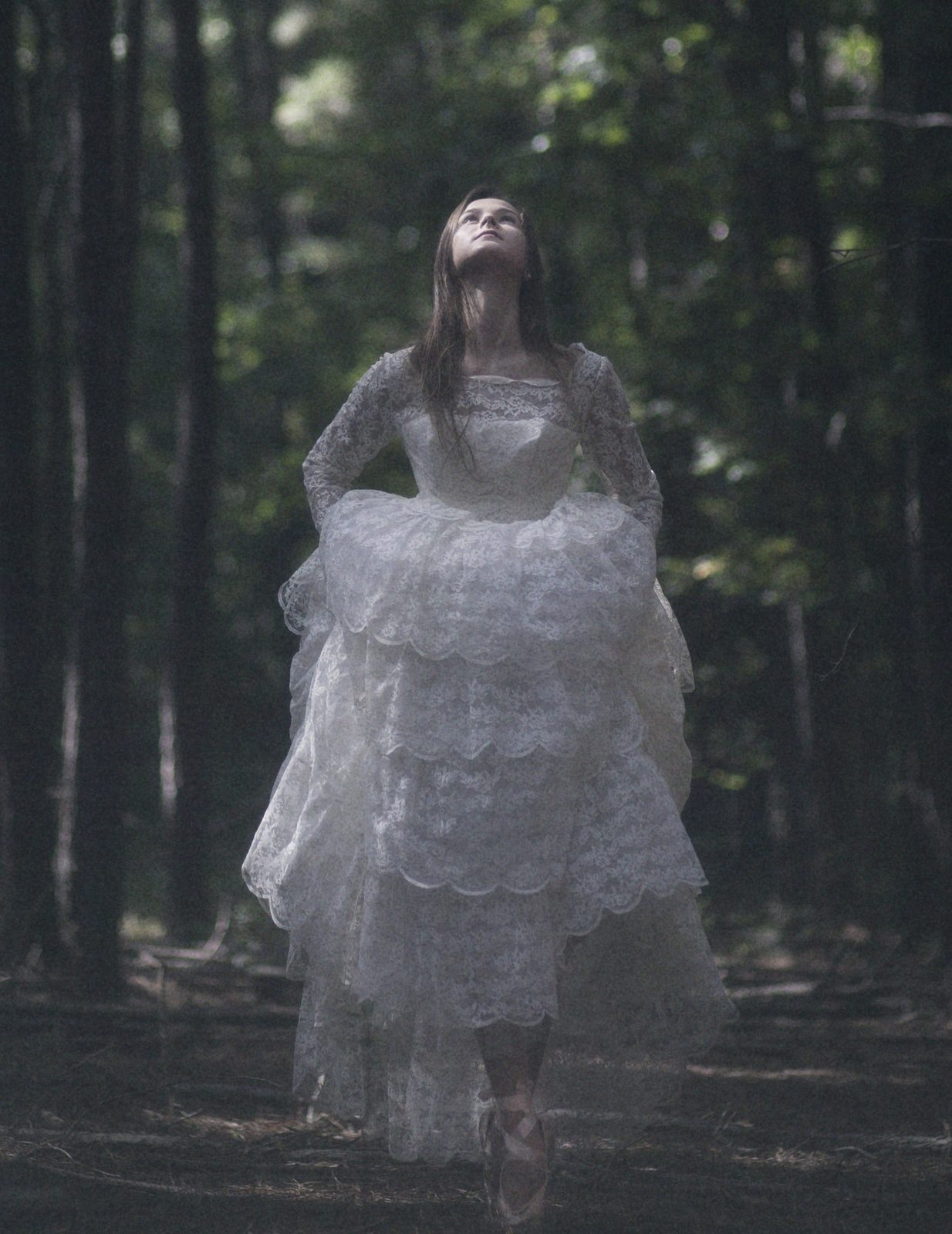 Model in a tiered white lace gown looks up toward the treetops
