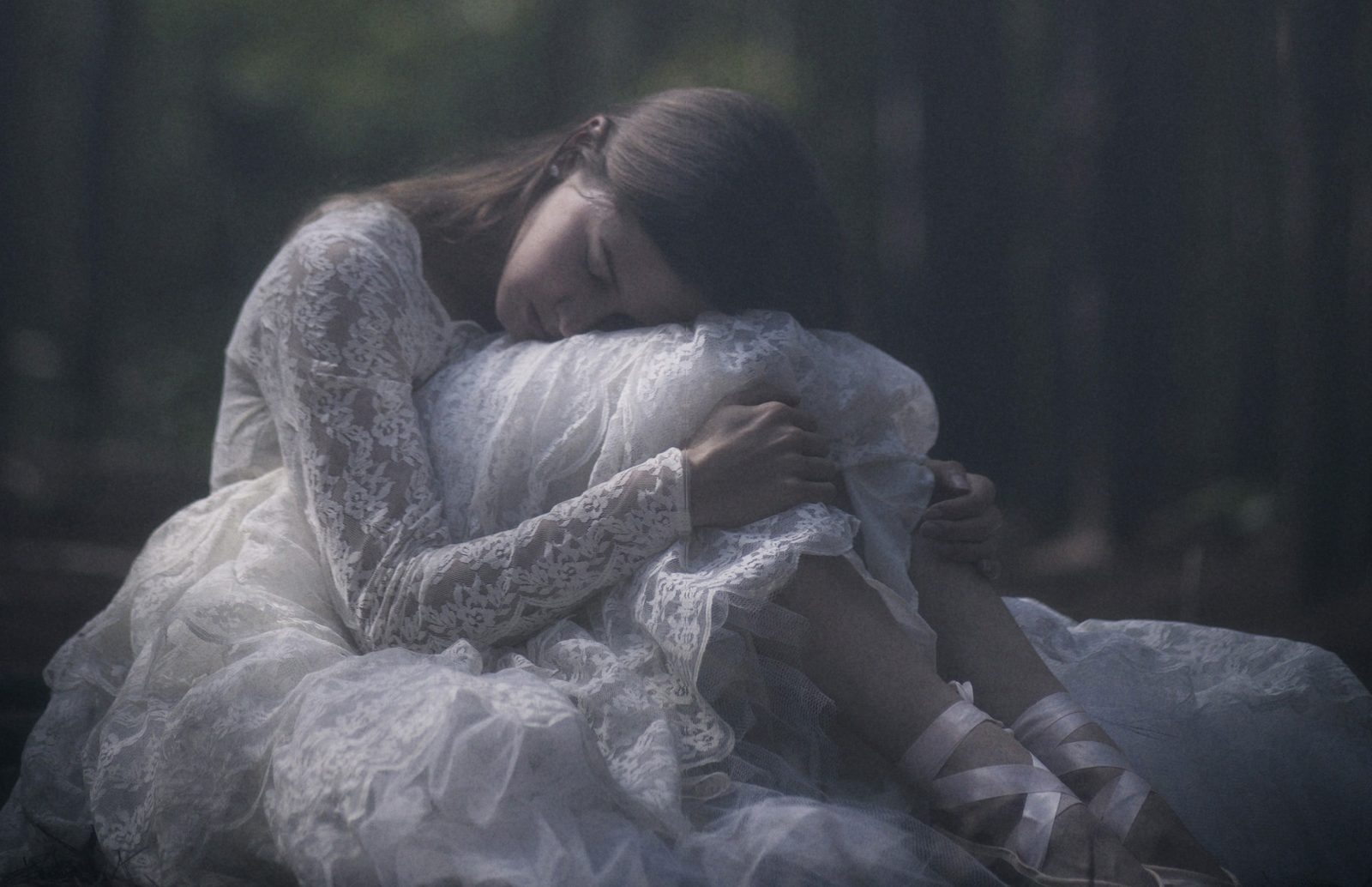 Model in a white lace gown rests her head on a pile of tulle, ballet ribbons laced up her ankles