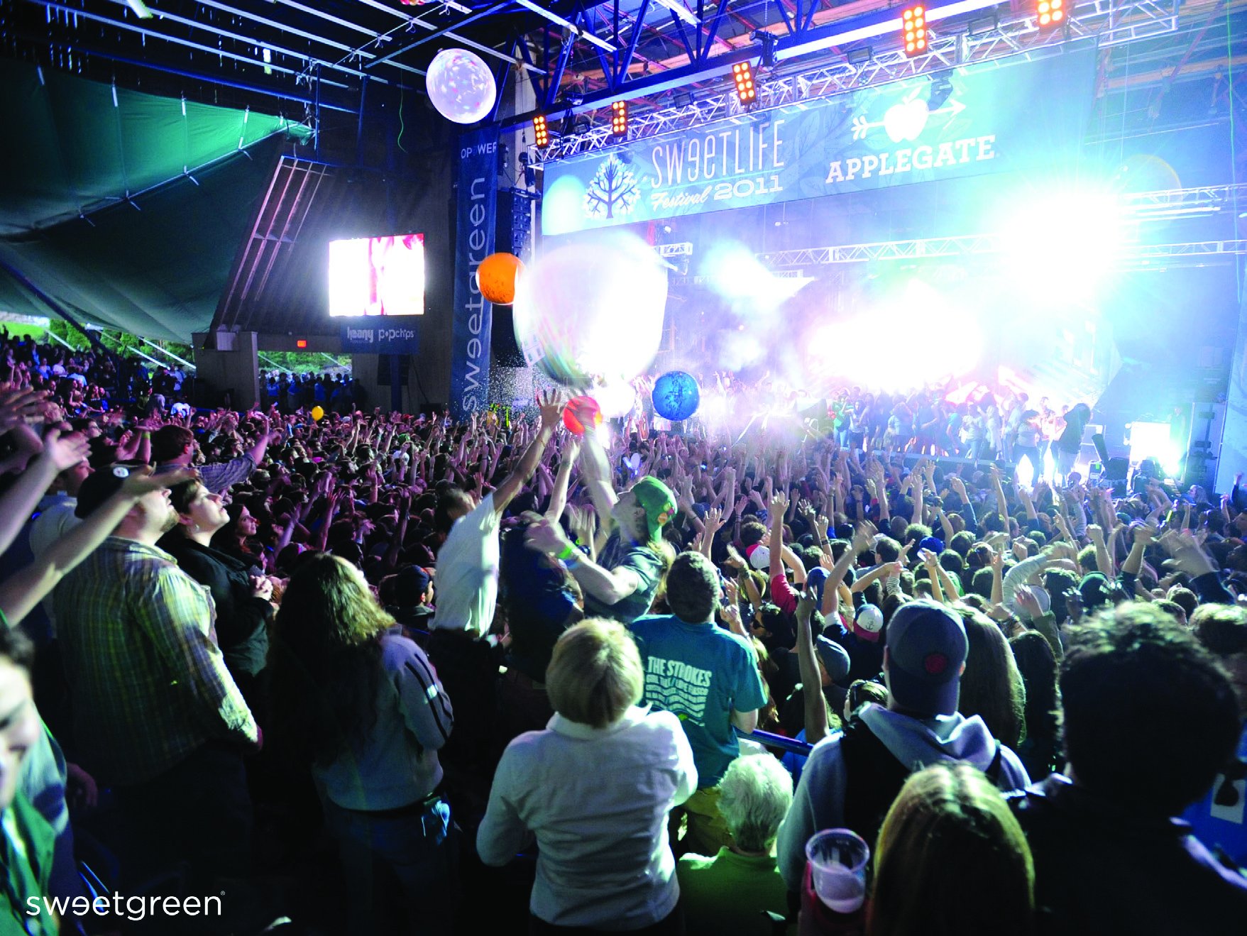 Crowd with hands in the air facing a brightly lit festival stage hung with Sweetlife and Sweetgreen banners