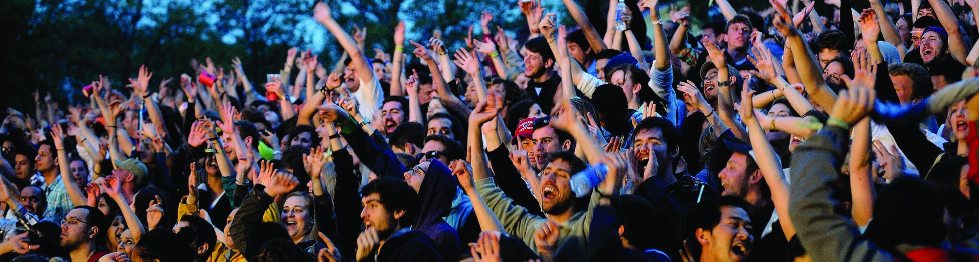 Packed festival crowd cheering with arms raised in front of the stage