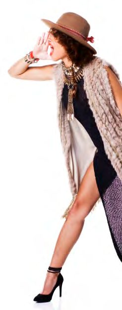 Model in a wide-brim hat, layered necklaces and a long shaggy vest over a patterned dress, shouting with one hand cupped to her mouth