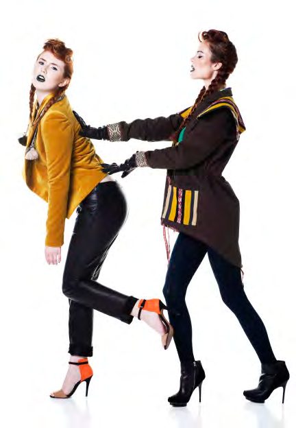 Two models in punk makeup tugging at each other, one in a mustard blazer and leather pants, the other in a brown anorak and zigzag skirt