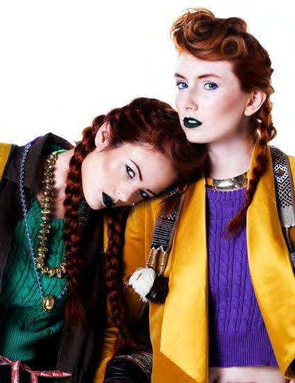 Two models with braids and green lipstick leaning head to head in a green crop sweater and a mustard blazer with Peruvian textiles