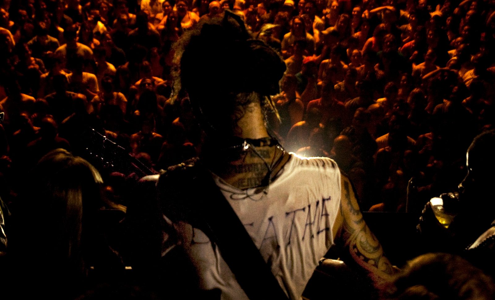 Michael Franti seen from behind on stage facing a packed, warmly lit crowd