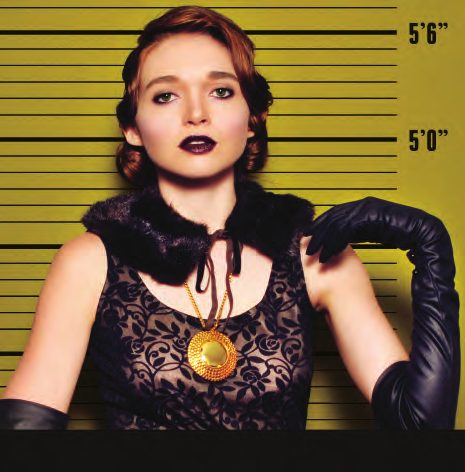 Mug shot of a model with a vintage updo, plum lips, black lace, a fur collar and black opera gloves against an olive height chart