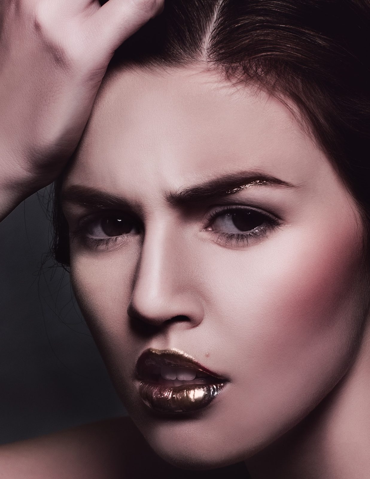 Model with a hand in her hair, furrowed brow and a high-shine metallic brown lip