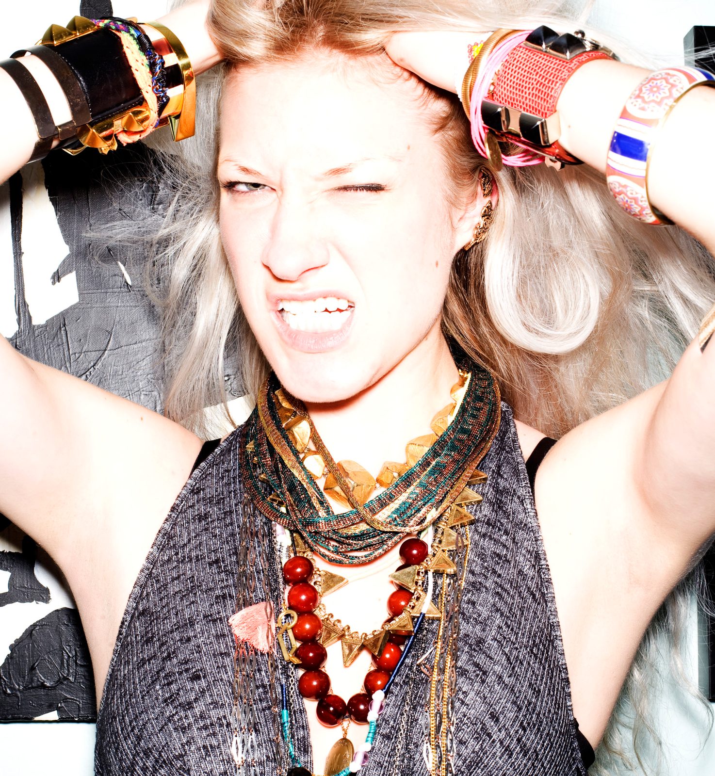 Maia Wojcik grimacing playfully with both hands in her tousled hair, piled with chunky beaded necklaces and cuffs
