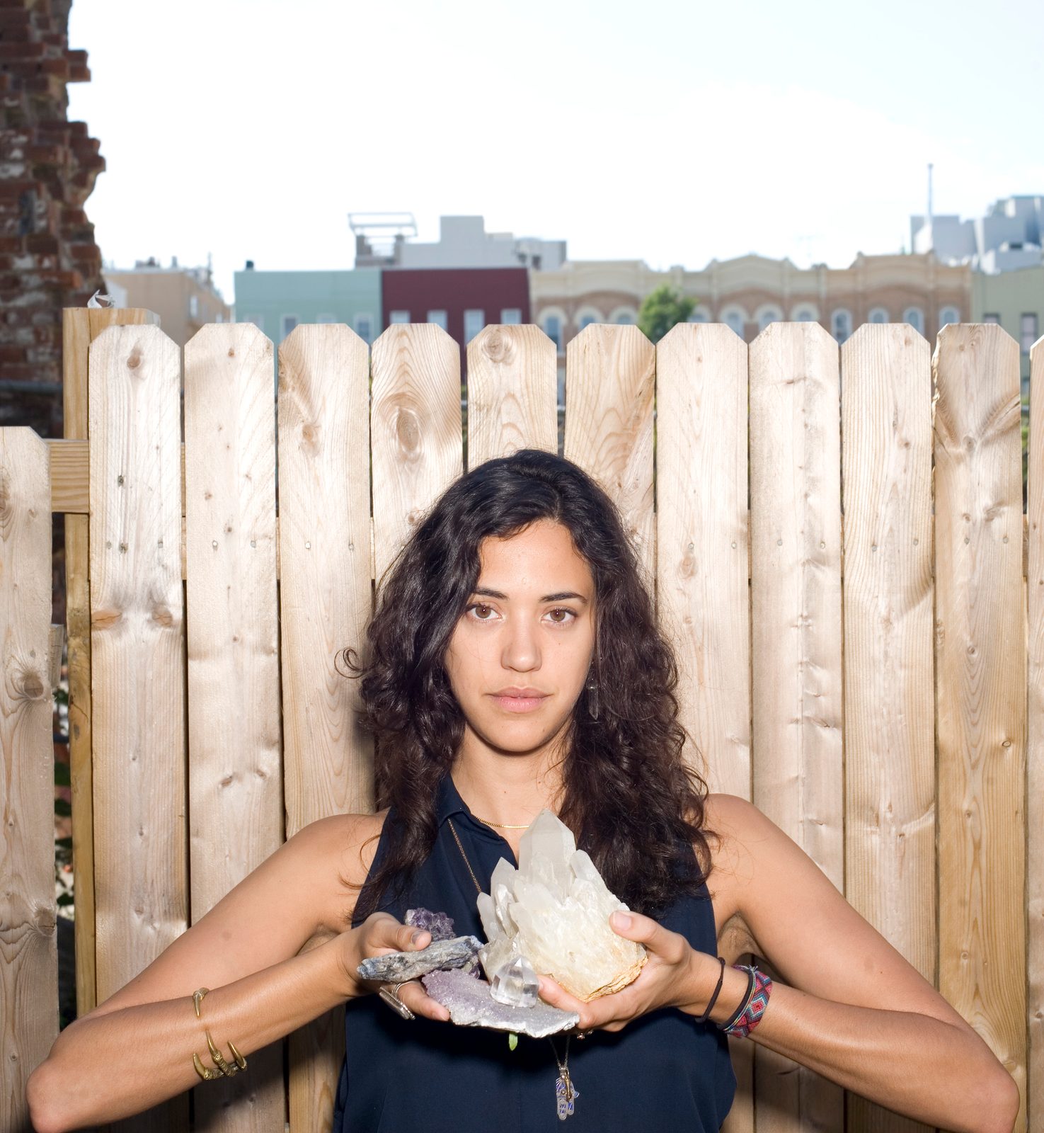 Yara Flinn holding a large clear quartz crystal cluster in front of a wooden fence on a rooftop