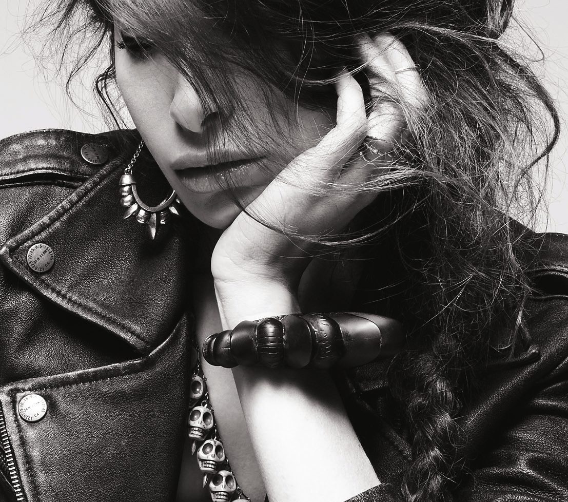 Black and white close-up of Pamela Love resting her head on her hand, wearing spiked rings and a leather jacket