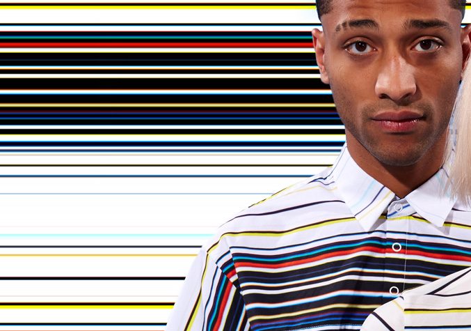 Male model in a white shirt with multicolored horizontal stripes against a striped graphic background