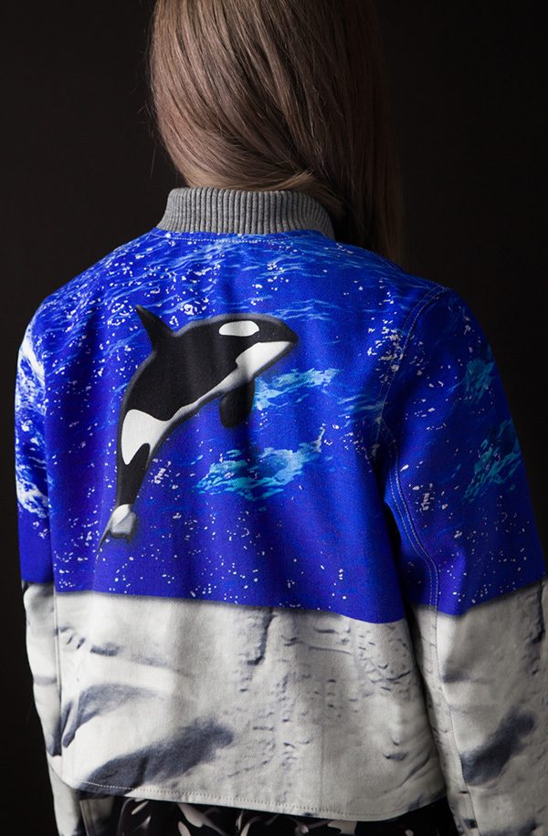 Back view of a model in a cobalt and white jacket printed with an orca leaping over icy water