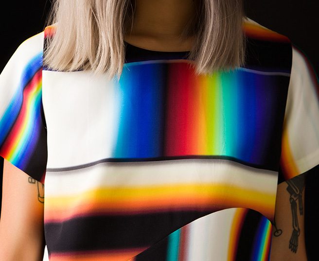 Close crop of a short sleeve top printed with distorted rainbow prismatic stripes