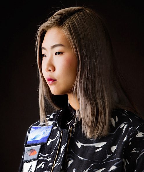 Portrait of a model with long ash blond hair in a black and white printed jacket with photo print patches