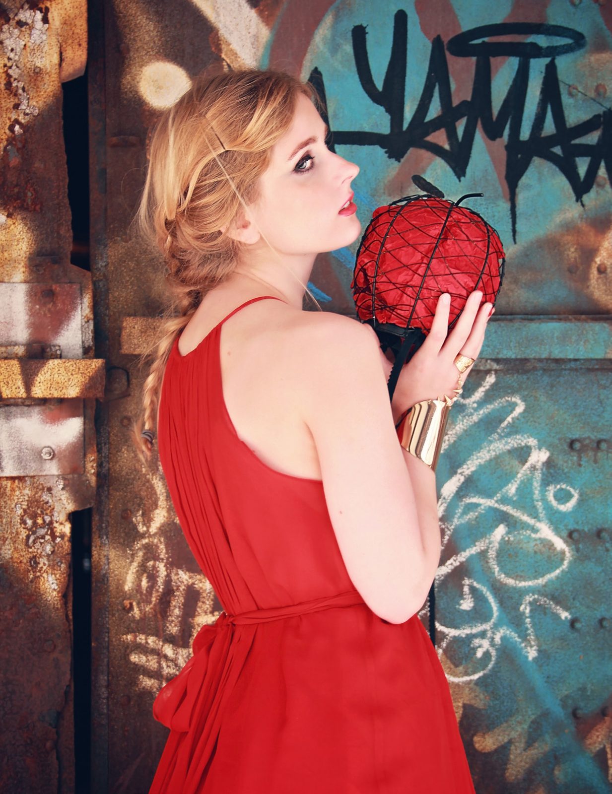 Model in a red halter gown holds a red lattice orb against a graffiti-covered wall