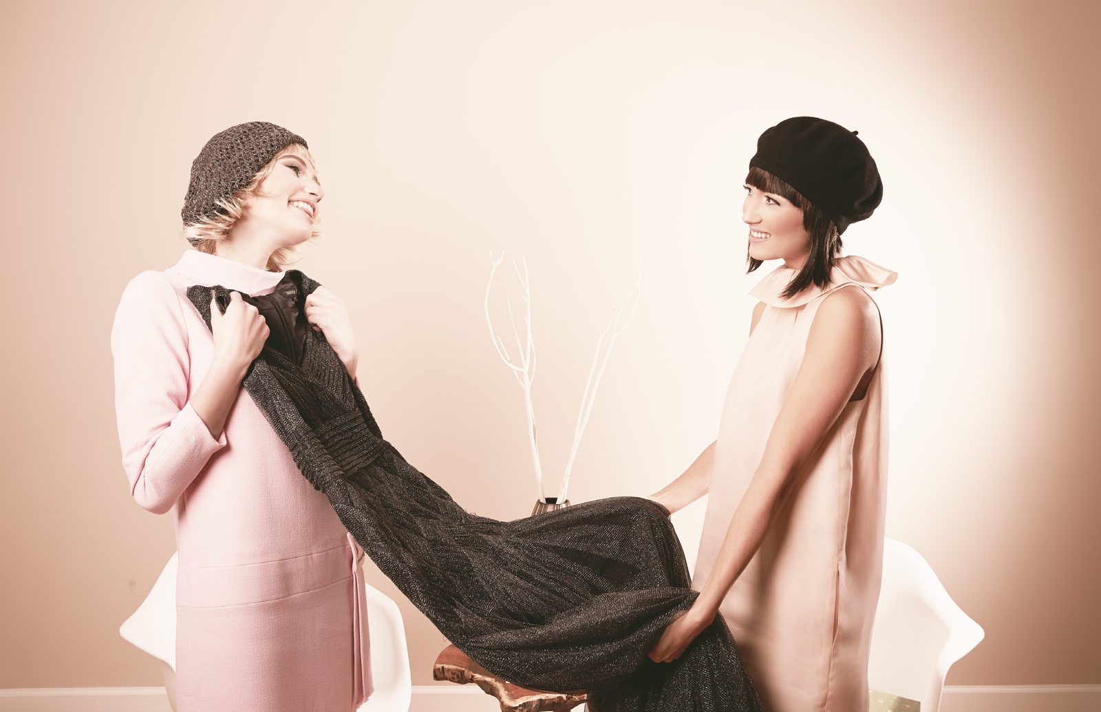 Two models in berets tug a long black sequined gown between them, laughing