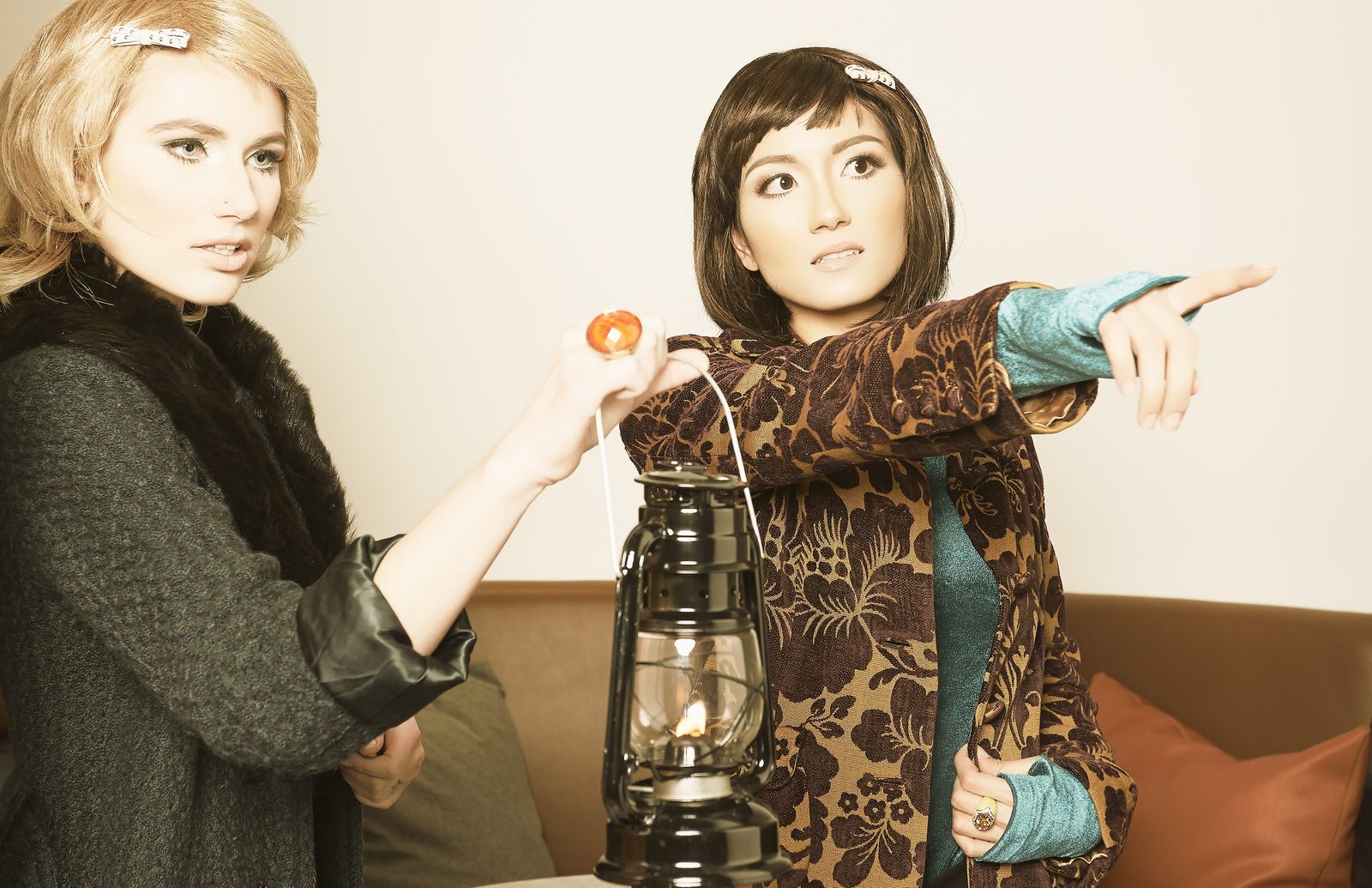 Model in a fur-collared coat and a model in a brocade jacket share a lantern, one pointing off frame