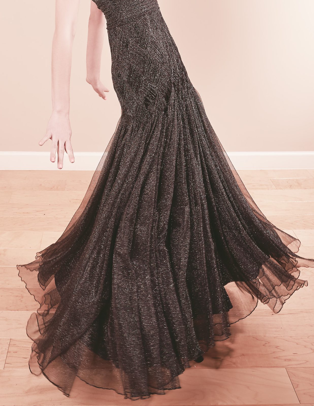 Model's arm and the flared tulle hem of a long black gown on a wood floor