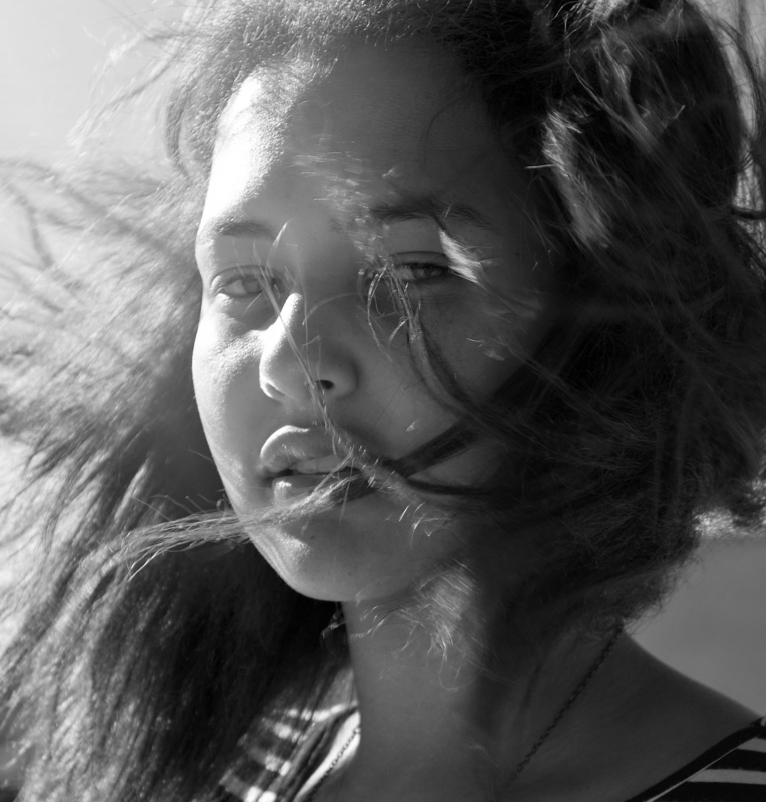 Black and white close portrait of a young woman with dark hair blowing across her face