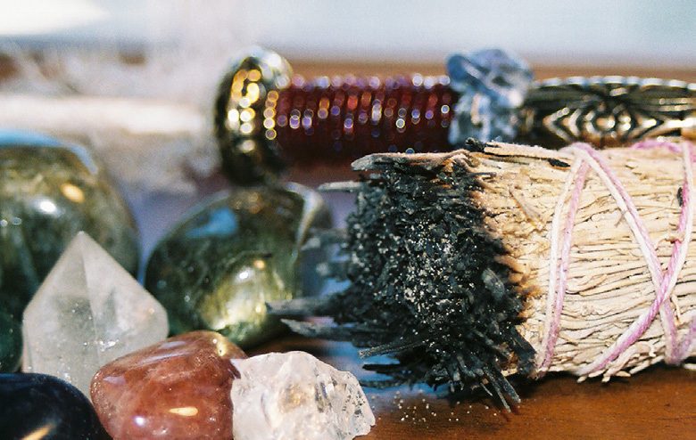 Crystals, a bundle of dried sage and a decorated wand laid out on a table