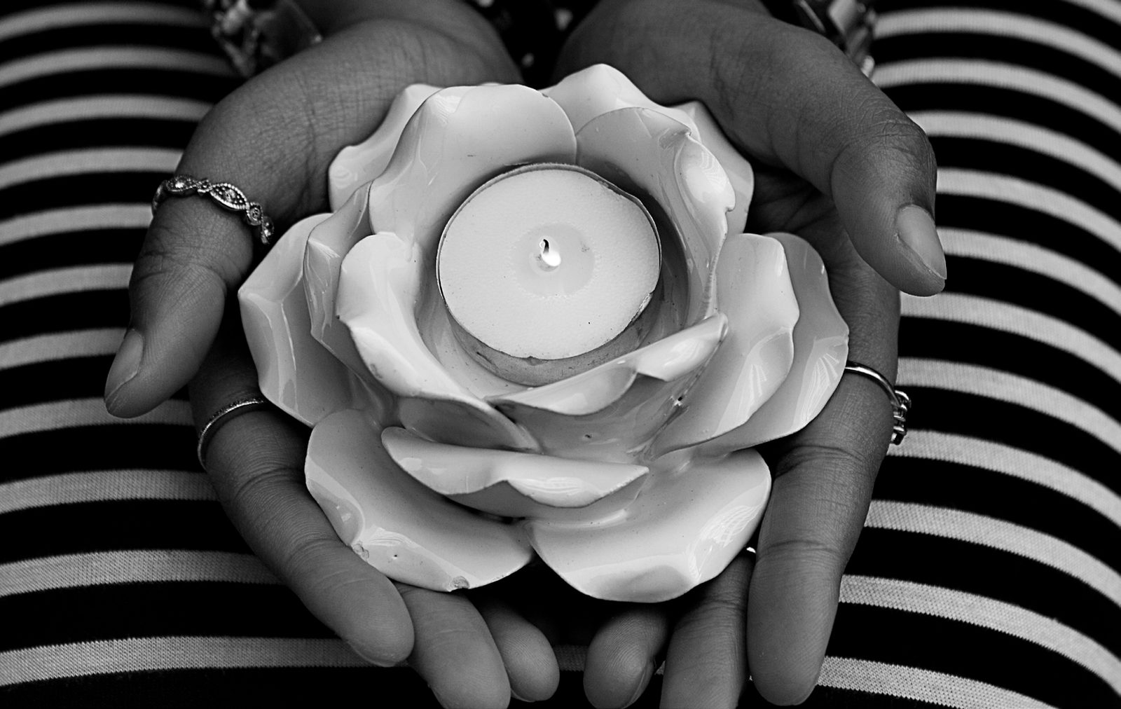 Hands with silver rings cradle a white lotus-shaped candle holder with a lit tea light, in black and white