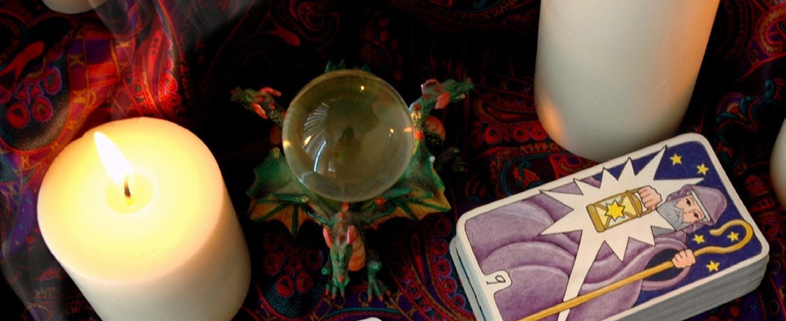 A lit pillar candle, a crystal ball and a Tarot deck on a paisley cloth