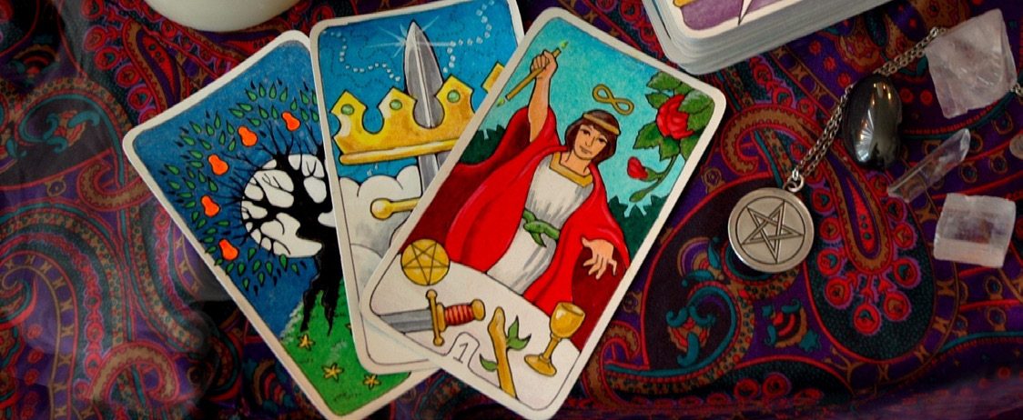 Tarot cards fanned out on a paisley cloth beside a pentacle pendant and crystals
