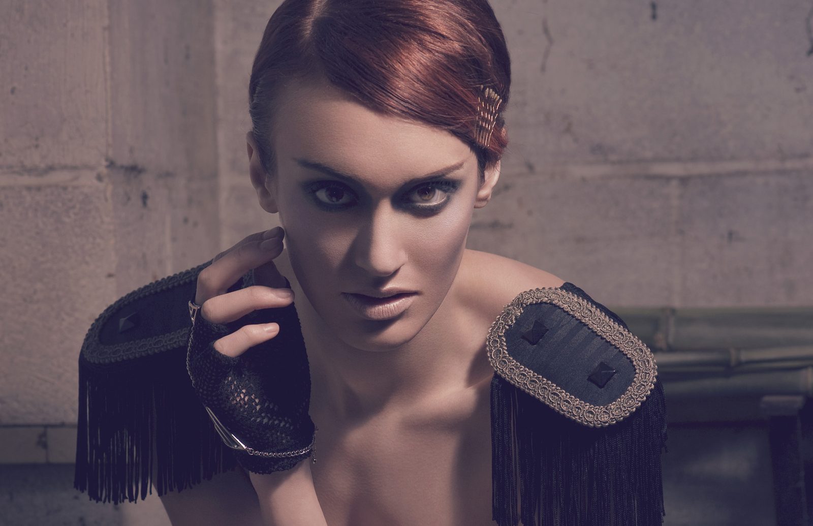 Model in fringed black military epaulets and a fingerless leather glove, hand at her collarbone