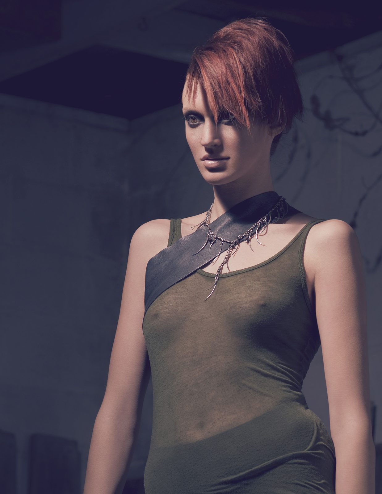 Model in a sheer olive tank with a black leather harness strap across the chest