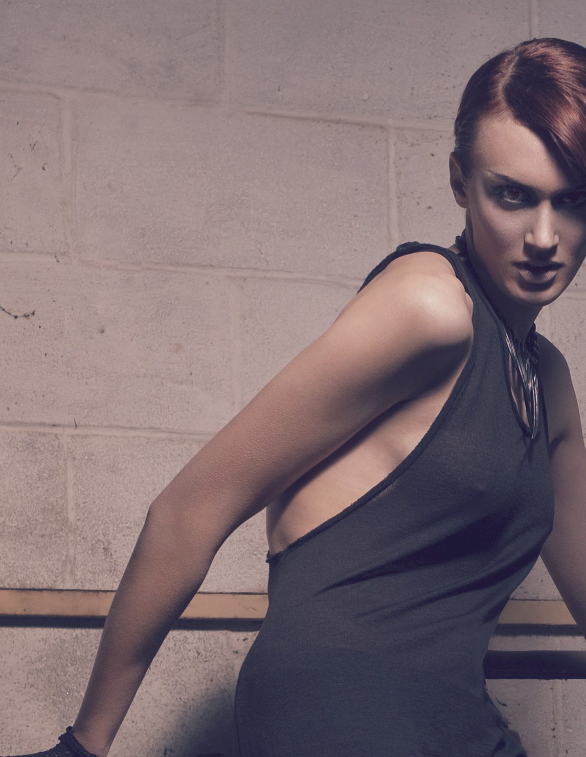 Model in a charcoal halter dress with an open back, glancing over her shoulder