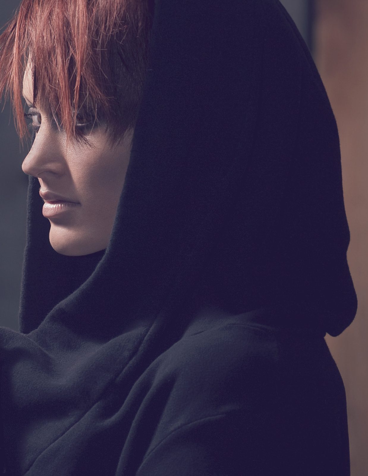 Profile of the model in an oversized black hood, copper fringe falling over her eyes