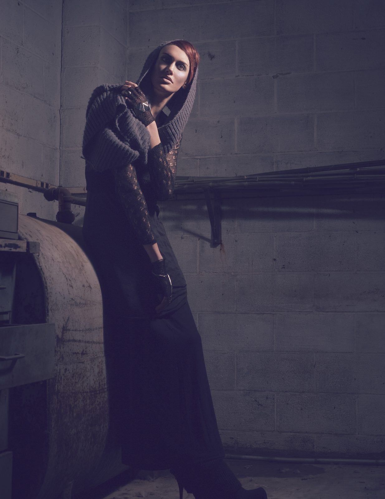 Full-length shot of the model in a long black layered look standing beside an old boiler