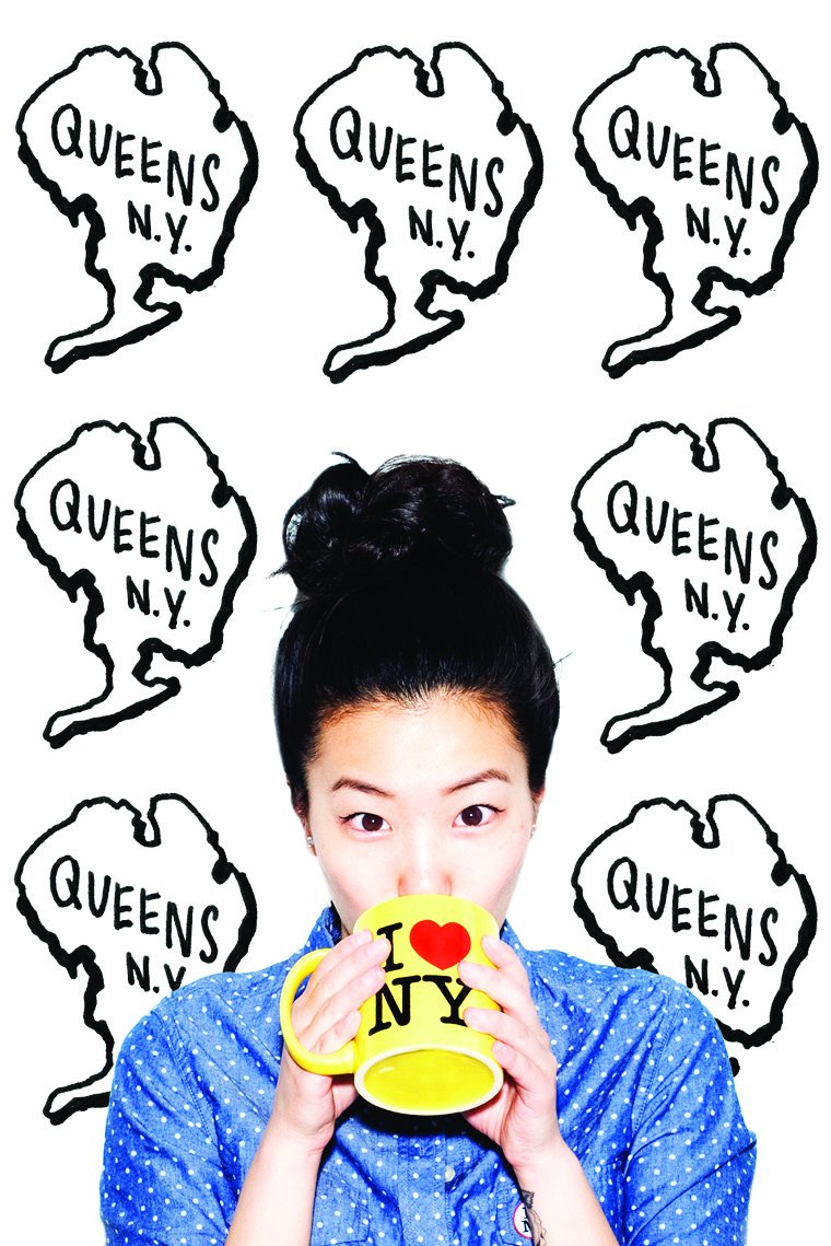 Sophia Chang sipping from an I Love NY mug in front of a wall of hand-drawn Queens N.Y. graphics